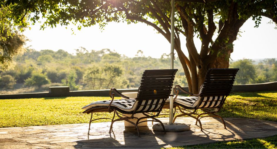 Two sun loungers under a shady tree overlooking the tranquil African bush at Anantara Stanley & Livingstone Boutique Hotel.