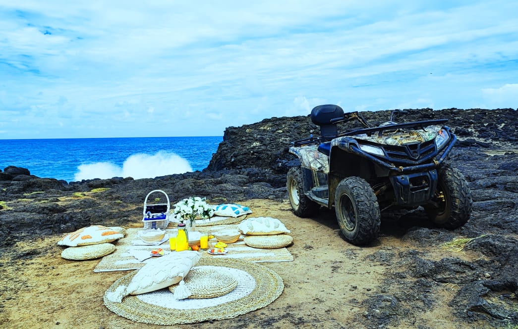 A coastal picnic with a picturesque ocean view, featuring cushions, a spread of snacks and a parked ATV.