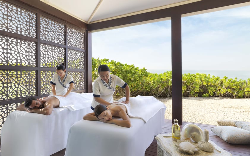 A couple, man and woman, lying face down and receiving a massage from their respective masseuses.