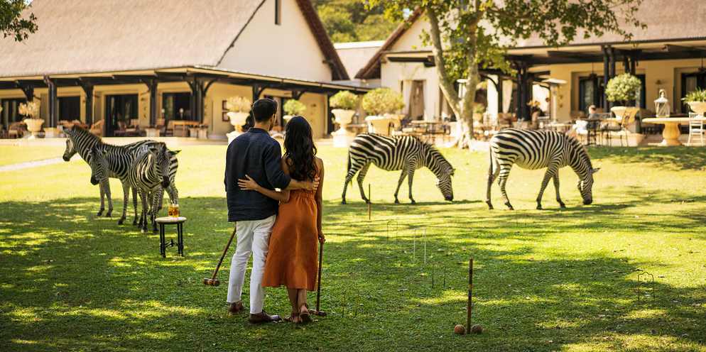A couple playing croquet with the hotel and zebra in the background.