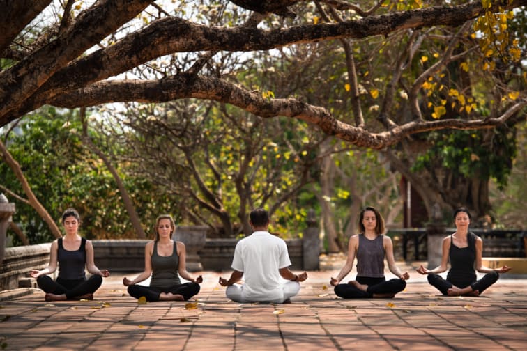 Four students and an instructor sit and meditate beneath the trees at the pagoda.