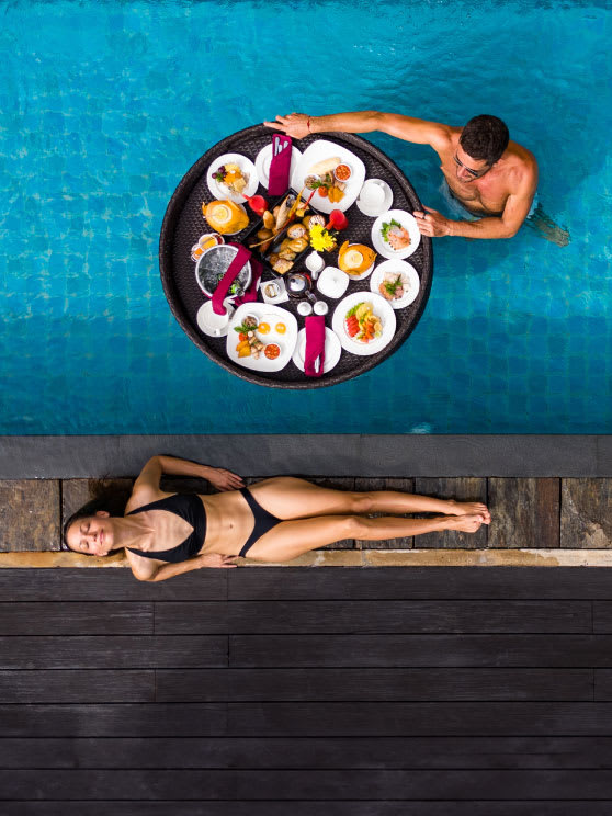 A girl and a guy with a floating breakfast by the pool